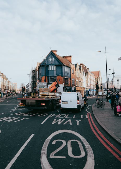 A flatbed truck fitted with a hydraulic lift, parked on a busy city street at Dalston Junction during daylight, used for home relocation or furniture transport by Man With a Van Shacklewell. The truck