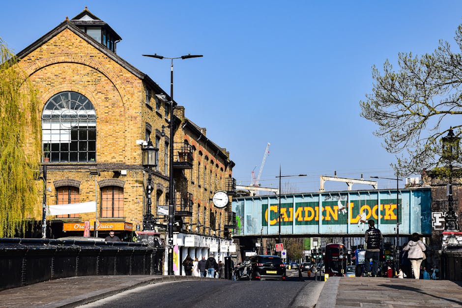 A flatbed truck fitted with a hydraulic lift, parked on a busy city street at Dalston Junction during daylight, used for home relocation or furniture transport by Man With a Van Shacklewell. The truck